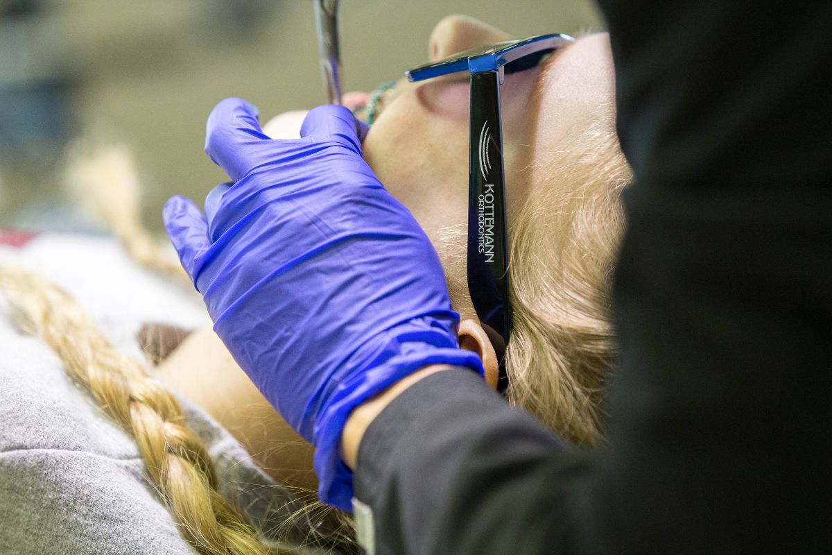 A person receives dental care while wearing protective glasses. A gloved hand works on their teeth. The environment is a dental office.