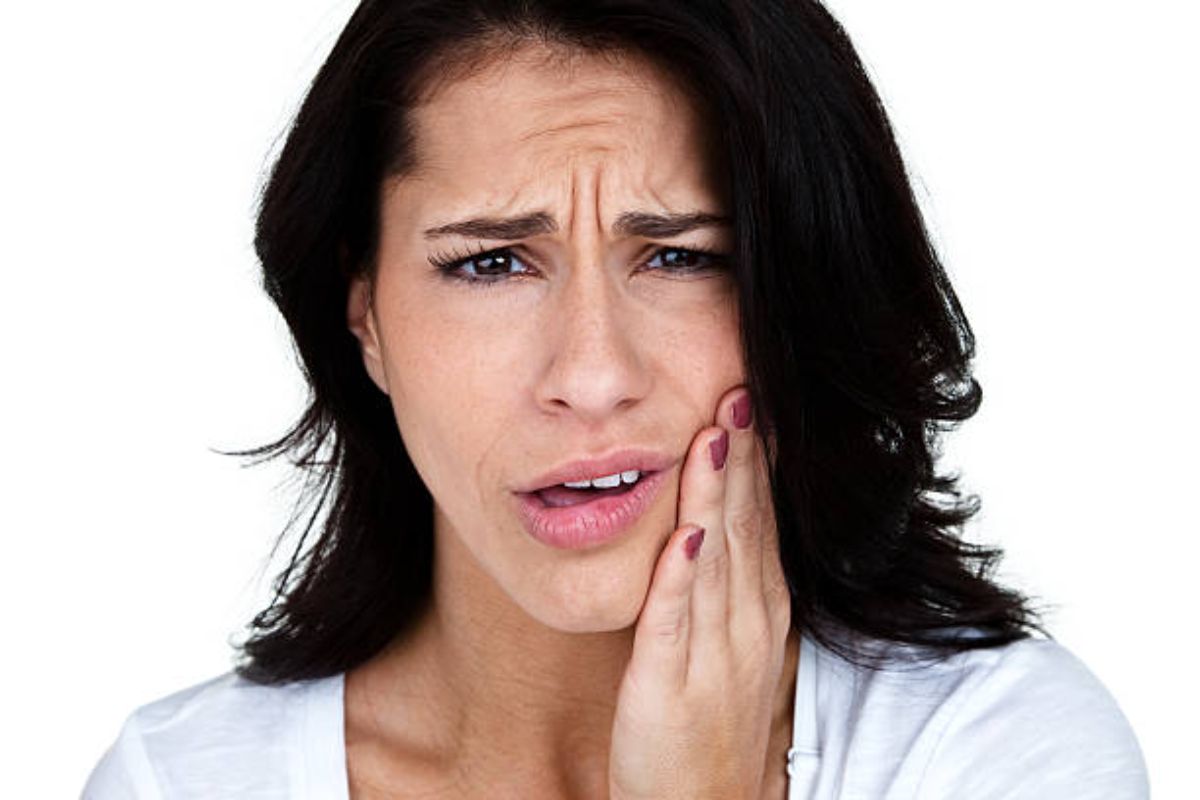 A person appears concerned, touching their cheek, possibly experiencing discomfort. The background is plain and white, offering no additional details or landmarks.