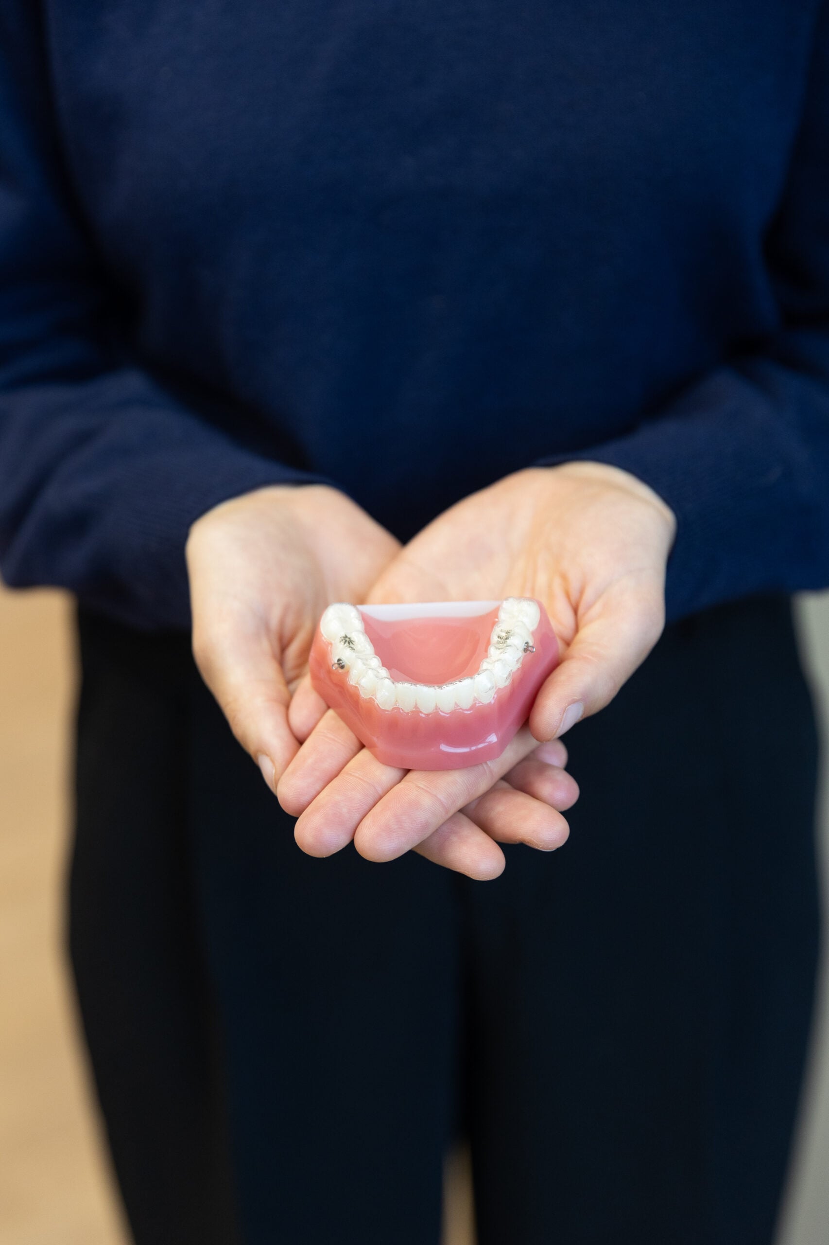 A person in a dark sweater holds a dental model of the lower jaw with orthodontic braces, emphasizing dental care or orthodontics.